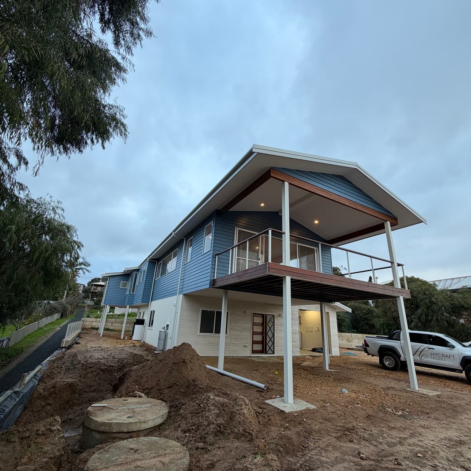 Two-storey coastal home painted in blue weatherboard with white trims and a balcony